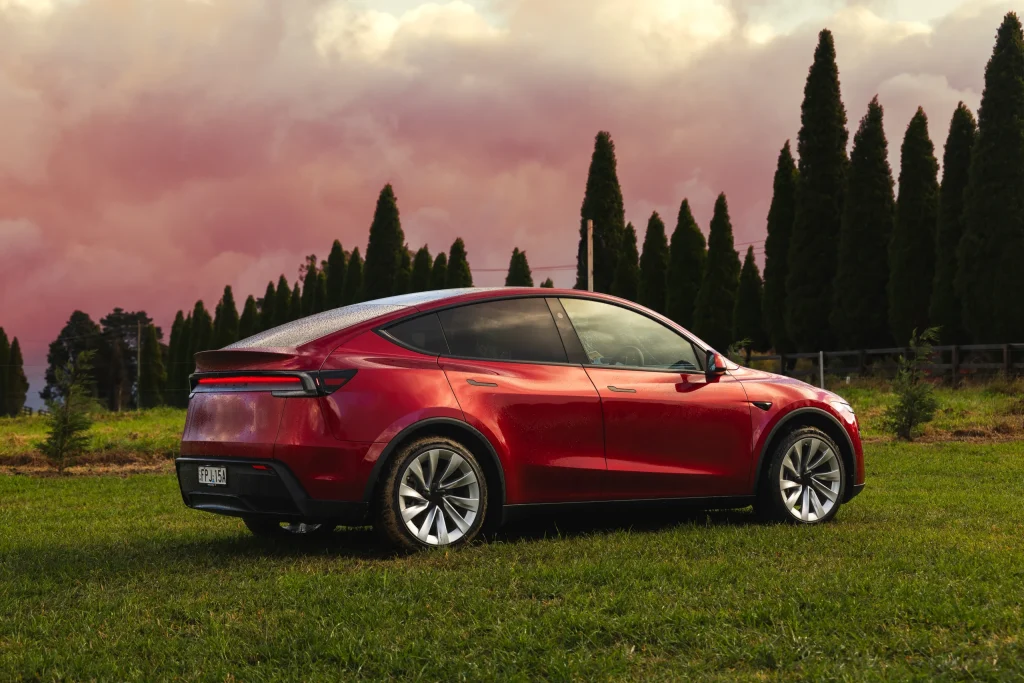 Red Tesla Model Y on grass at an outdoor press drive event