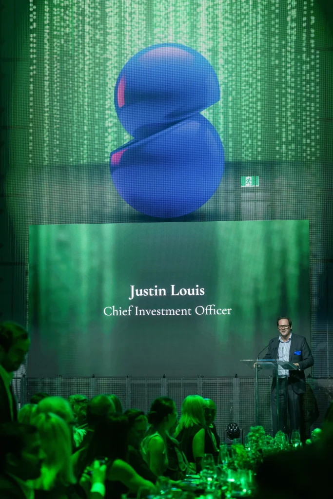 Justin Louis speaks at a lectern with his name and Chief Investment Officer title on the screen